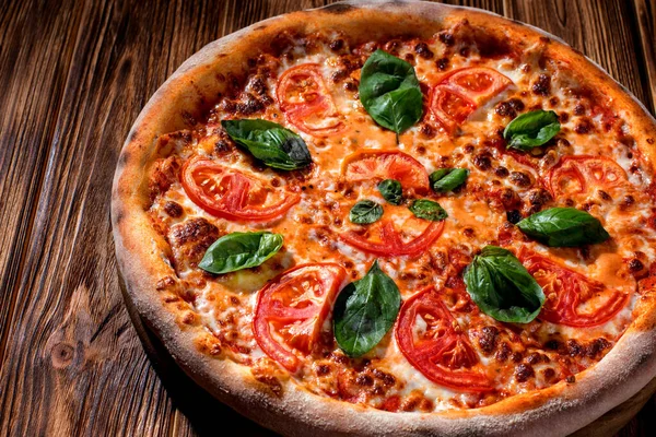 Delicious fragrant pizza with mozzarella, tomatoes and basil with tomato sauce on woden background.