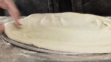 The pizzaiolo places the formed pizza dough on a tray. Cooking pizza in a pizzeria.