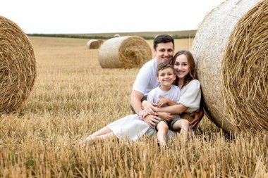Young family mom dad and son on the field near the straw bales. Family photo session.