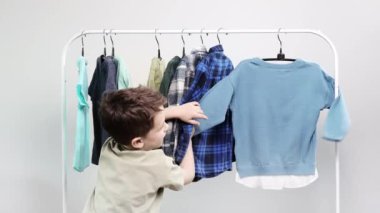 Boy preschooler standing by the hangers, racks up clothes, and chooses clothes fBoy preschooler standing by the hangers, racks up clothes, and chooses clothes for todayor today