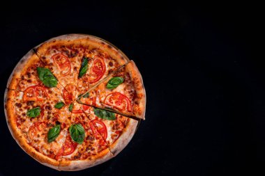 Delicious fragrant pizza-Margherita with mozzarella, tomatoes and basil on tomato sauce on black background. Copy space.