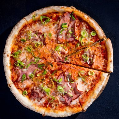 Delicious pizza with mozzarella cheese, ham, leeks on a tomato base on black background.