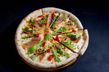 Pizza with jamon or prosciutto, mozzarella, cherry tomatoes, arugula and parmesan on a black background. Italian cuisine