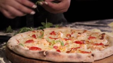 The chef decorates the freshly baked pizza with arugula. Cream-based pizza with salmon, mozzarella cheese, arugula, tomatoes, parmesan