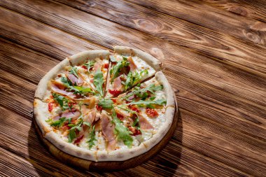 Pizza with jamon and prosciutto, mozzarella, cherry tomatoes, arugula and parmesan on a wood background. Italian cuisine