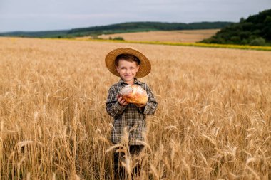 Little boy in the straw hat and shirt he held out his handing with bread in ripe grain. concept poverty, crisis, famine.