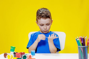 Küçük bir anaokulu öğrencisi elinde fırçayla masada oturur ve avucunu boyar. Anaokulu geliştirme