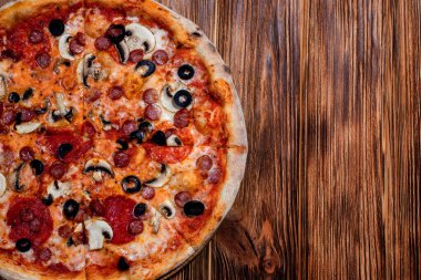 Tomato-based pizza with mozzarella cheese, hunting sausages, salami, olives, mushroom sauce. On a wooden background. Copy space.