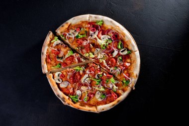 Vegan pizza with tomato sauce, cherry tomatoes, mushrooms, broccoli, red onion on black background. View from above.