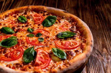 Delicious fragrant pizza with mozzarella, tomatoes and basil with tomato sauce on woden background.