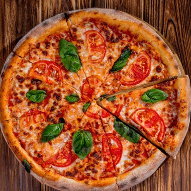 Delicious fragrant pizza-Margherita with mozzarella, tomatoes and basil on tomato sauce on woden background. Copy space.