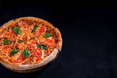 Delicious fragrant pizza-Margherita with mozzarella, tomatoes and basil on tomato sauce on black background. Copy space.