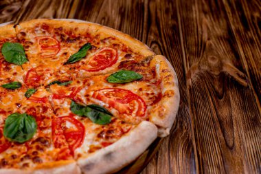 Delicious fragrant pizza-Margherita with mozzarella, tomatoes and basil on tomato sauce on woden background. Copy space.