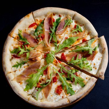 Pizza with jamon or prosciutto, mozzarella, cherry tomatoes, arugula and parmesan on a black background. Italian cuisine