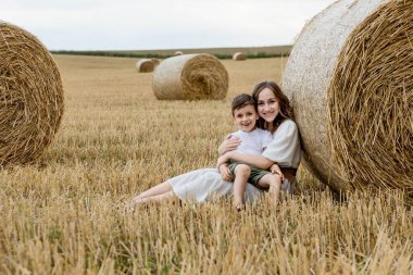 Genç anne ve oğlu bir tarlada saman balyalarının yanında sarılıyorlar. Mutlu bir aile. Anneler Günü..