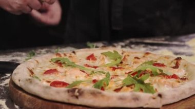 The chef decorates the freshly baked pizza with arugula. Cream-based pizza with salmon, mozzarella cheese, arugula, tomatoes, parmesan