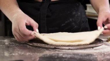 The pizzaiolo places the formed pizza dough on a tray. Cooking pizza in a pizzeria.