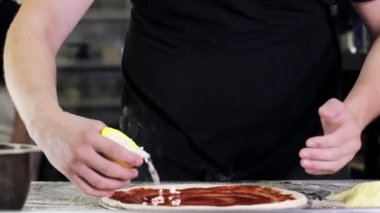 Chef sprinkles pizza with mozzarella cheese in the kitchen of a pizzeria. Pizza to order. Cooking pizza.