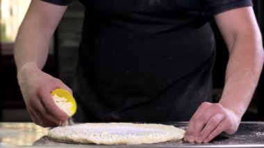 Chef sprinkles pizza with mozzarella cheese in the kitchen of a pizzeria. Pizza to order. Cooking pizza.