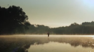 Fisherman pulling fish on the river in a foggy summer morning. Fishing for spinning.
