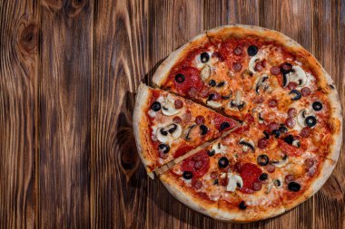 Tomato-based pizza with mozzarella cheese, hunting sausages, salami, olives, mushroom sauce. On a wooden background. Copy space.