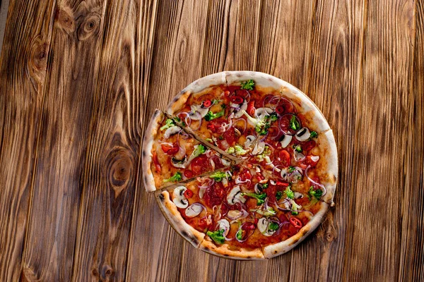 Vegan pizza with tomato sauce, cherry tomatoes, mushrooms, broccoli, red onion on wodenbackground. View from above.