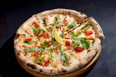 Pizza with salmon, mozzarella, cherry tomatoes, arugula, lemon and parmesan. Italian cuisine. On a black background