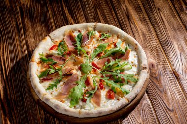 Pizza with jamon and prosciutto, mozzarella, cherry tomatoes, arugula and parmesan on a wood background. Italian cuisine
