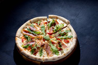 Pizza with jamon or prosciutto, mozzarella, cherry tomatoes, arugula and parmesan on a black background. Italian cuisine