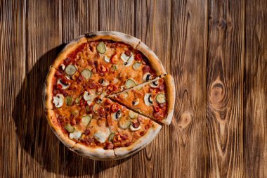 Appetizing pizza with hunting sausages, mozzarella cheese, pickled cucumbers, chili peppers on a tomato base on wood background.