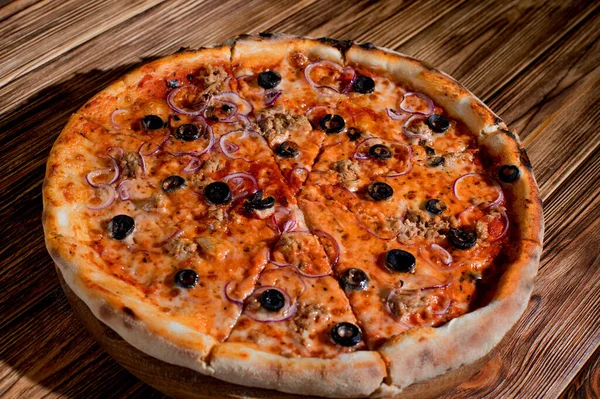 Pizza with tuna, olives, onions, mozzarella cheese and tomato sauce on wood background. Top view, copy space.