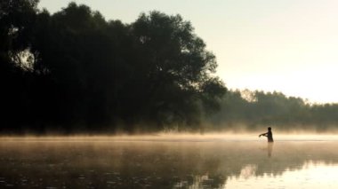 Fisherman pulling fish on the river in a foggy summer morning. Fishing for spinning.