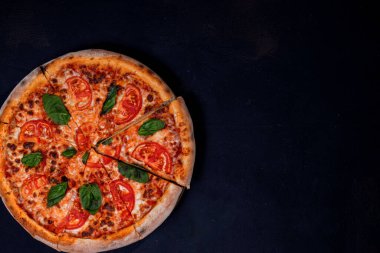 Delicious fragrant pizza-Margherita with mozzarella, tomatoes and basil on tomato sauce on black background. Copy space.