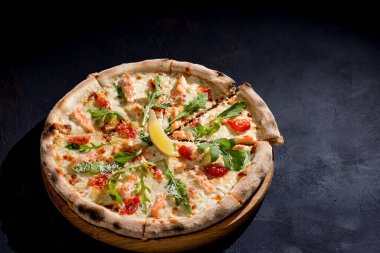 Pizza with salmon, mozzarella, cherry tomatoes, arugula, lemon and parmesan. Italian cuisine. On a black background. Free space for text. View from above