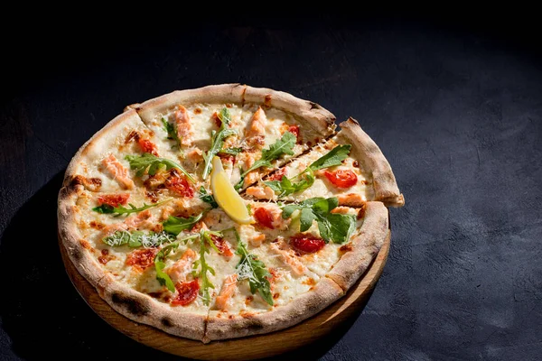 Pizza with salmon, mozzarella, cherry tomatoes, arugula, lemon and parmesan. Italian cuisine. On a black background. Free space for text. View from above