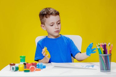Küçük bir anaokulu öğrencisi masada oturuyor, avuç içlerini bir kağıt parçasına çiziyor. Renkli el izleri. Anaokulu geliştirme.