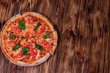 Delicious fragrant pizza-Margherita with mozzarella, tomatoes and basil on tomato sauce on woden background. Copy space.