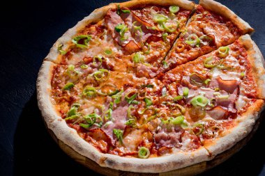 Delicious pizza with mozzarella cheese, ham, leeks on a tomato base on black background.