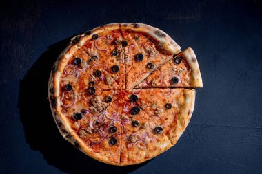 Pizza with tuna, olives, onions, mozzarella cheese and tomato sauce on a black background. Top view.