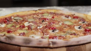 Appetizing pizza with hunting sausages, mozzarella cheese, pickled cucumbers, chili peppers on a tomato base on black background.