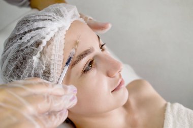 Genç bir kadına iğne yapan bir yüz verilir. Gençlik bakımı. Kozmetoloji. Yüzün güzelliği.