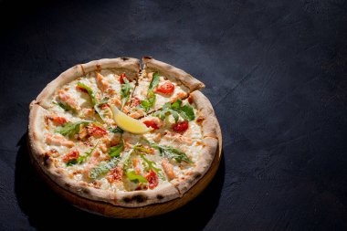 Pizza with salmon, mozzarella, cherry tomatoes, arugula, lemon and parmesan. Italian cuisine. On a black background. Free space for text. View from above