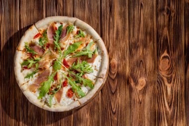 Pizza with jamon and prosciutto, mozzarella, cherry tomatoes, arugula and parmesan on a wood background. Italian cuisine
