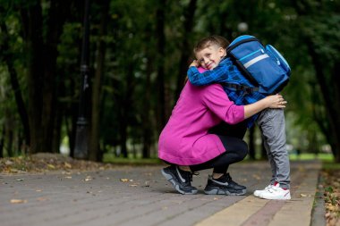 Genç bir kadın güneşli bir günde heyecanlı oğlunu birinci sınıfa götürüyor. Çalışmaya hazır.