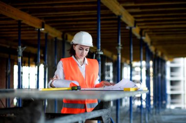 Mimar ya da mühendis, bina inşaatı projesini bina içinde ayrıntılı bir planla inceliyor. Kadın inşaat mühendisleri veya mimarlar çalışan insanlar.