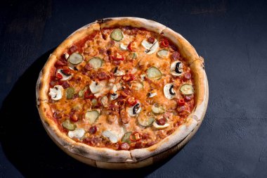 Appetizing pizza with hunting sausages, mozzarella cheese, pickled cucumbers, chili peppers on a tomato base. Mexican pizza. Top view.