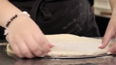The pizzaiolo places the formed pizza dough on a tray. Cooking pizza in a pizzeria.