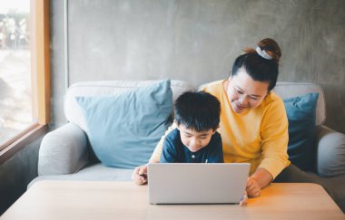 Anne ve oğlu, COVID 19 tecridi sırasında bilgisayarını kullanarak bir kafede ders çalışırken ekranda bir şey izliyorlar. Çevrimiçi Eğitim, Ev Okulu.