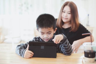 Anne, oğlu internette okurken beş yaşındaki oğlunu cesaretlendiriyor. Asyalı bir anne, küçük oğluna kafede e-öğrenim dersleri veriyor. Öğrenmek için tablet kullanan çocuk.