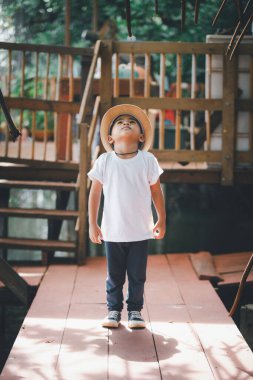 Yakışıklı dört yaşındaki Taylandlı çocuk beyaz bir tişört, şapka giy, ayağa kalk ve bak..